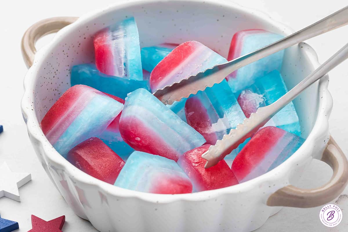 layered red white blue ice cubes in bowl with serving tongs