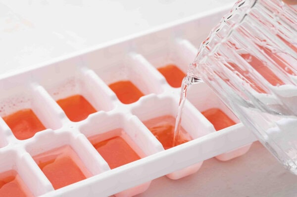 white liquid poured over red liquid in ice cube tray