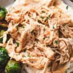 A plate of tender shredded chicken served with gravy over mashed potatoes, with green beans on the side.