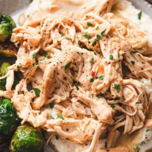 A plate of tender shredded chicken served with gravy over mashed potatoes, with green beans on the side.