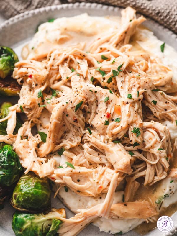 A plate of tender shredded chicken served with gravy over mashed potatoes, with green beans on the side.