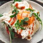 A top-down view of two crispy cheese nest eggs topped with herbs, served in a black skillet.