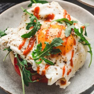 A top-down view of two crispy cheese nest eggs topped with herbs, served in a black skillet.