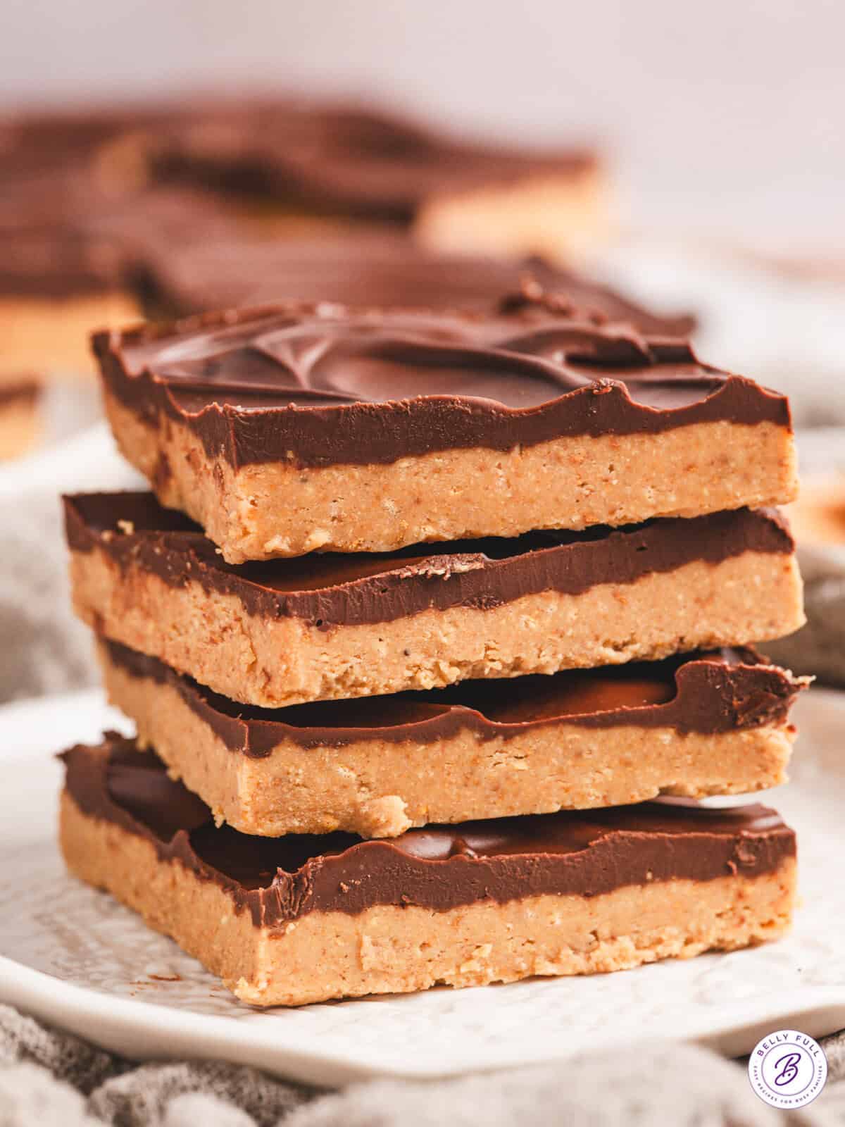 A stack of rich, chocolate-topped no-bake buckeye bars on a white surface, with one bar slightly offset to reveal the creamy peanut butter layer.