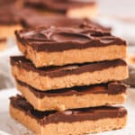 A stack of rich, chocolate-topped no-bake buckeye bars on a white surface, with one bar slightly offset to reveal the creamy peanut butter layer.