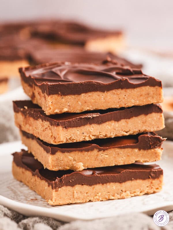 A stack of rich, chocolate-topped no-bake buckeye bars on a white surface, with one bar slightly offset to reveal the creamy peanut butter layer.