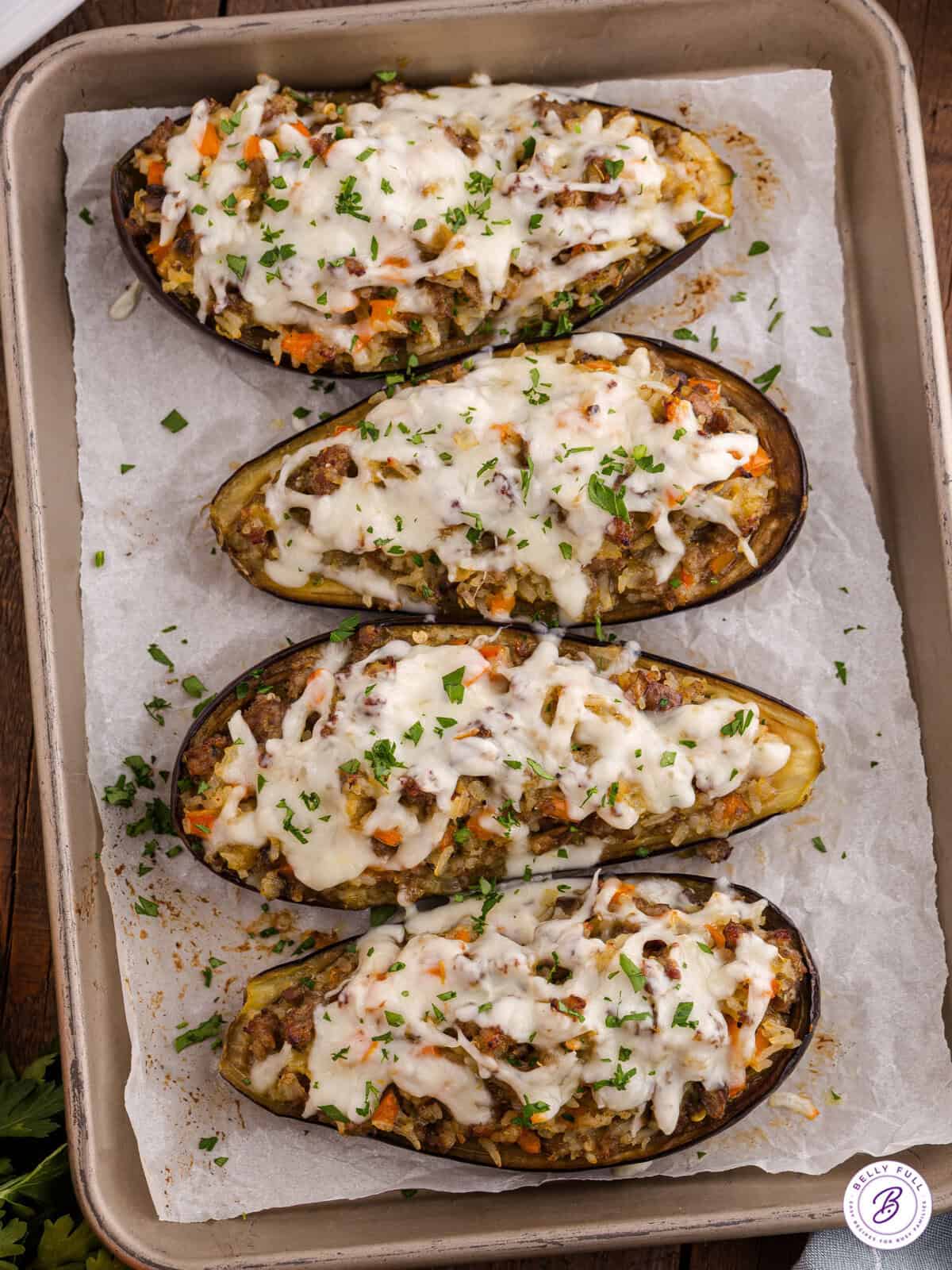 Baked stuffed eggplant halves filled with a golden breadcrumb and vegetable mixture, garnished with fresh parsley on a white plate.