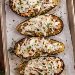 Baked stuffed eggplant halves filled with a golden breadcrumb and vegetable mixture, garnished with fresh parsley on a white plate.