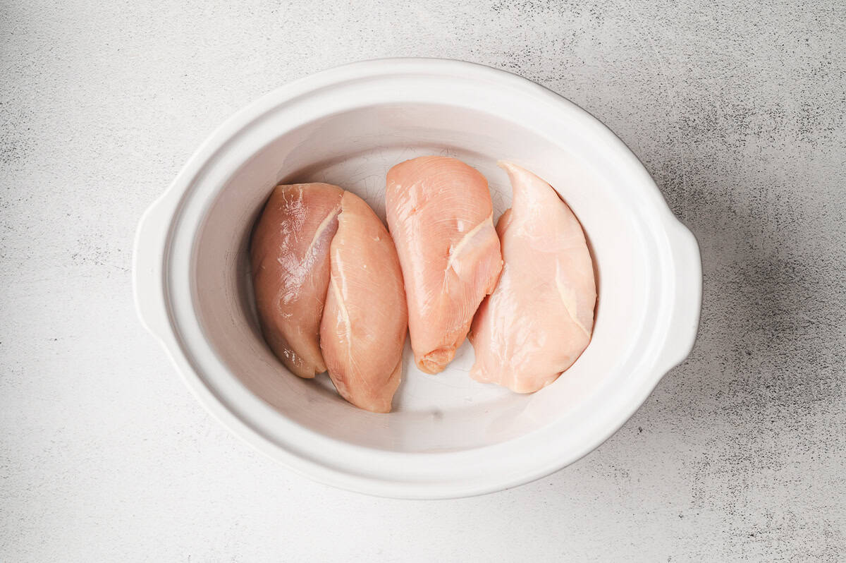 Raw chicken breasts placed in a slow cooker, ready to be seasoned.