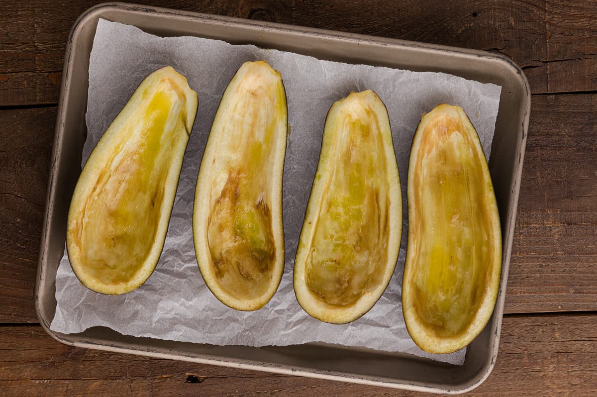Two halved eggplants on a cutting board with the flesh scored in a crisscross pattern.