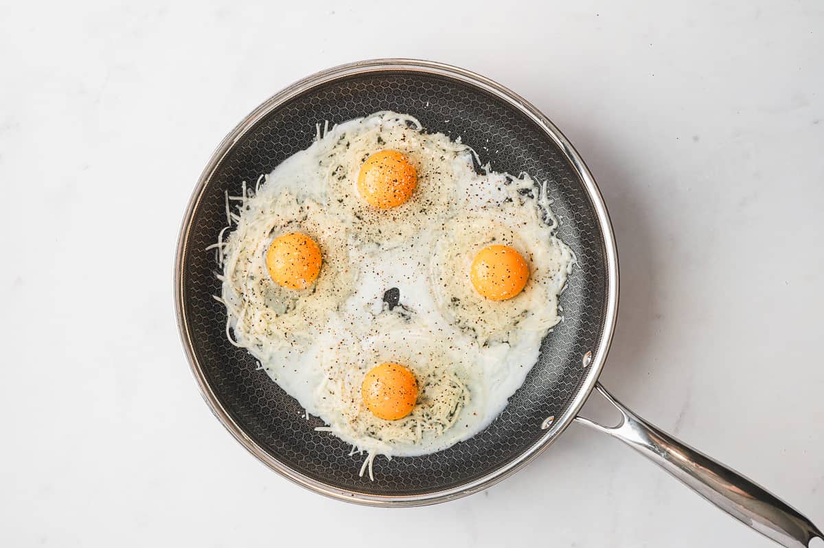 Cooked cheese nests in a skillet with an indentation in the center, ready for eggs.