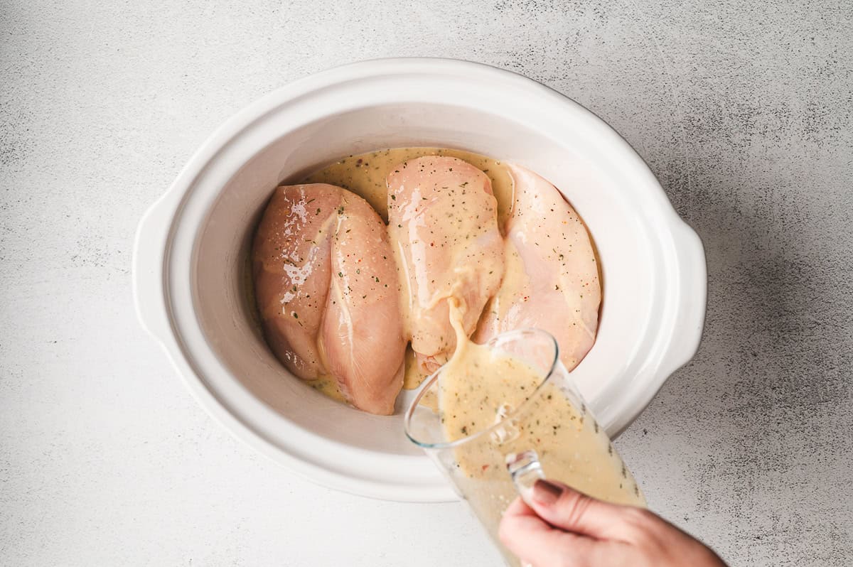 Slices of butter placed on top of the seasoned chicken in the slow cooker.