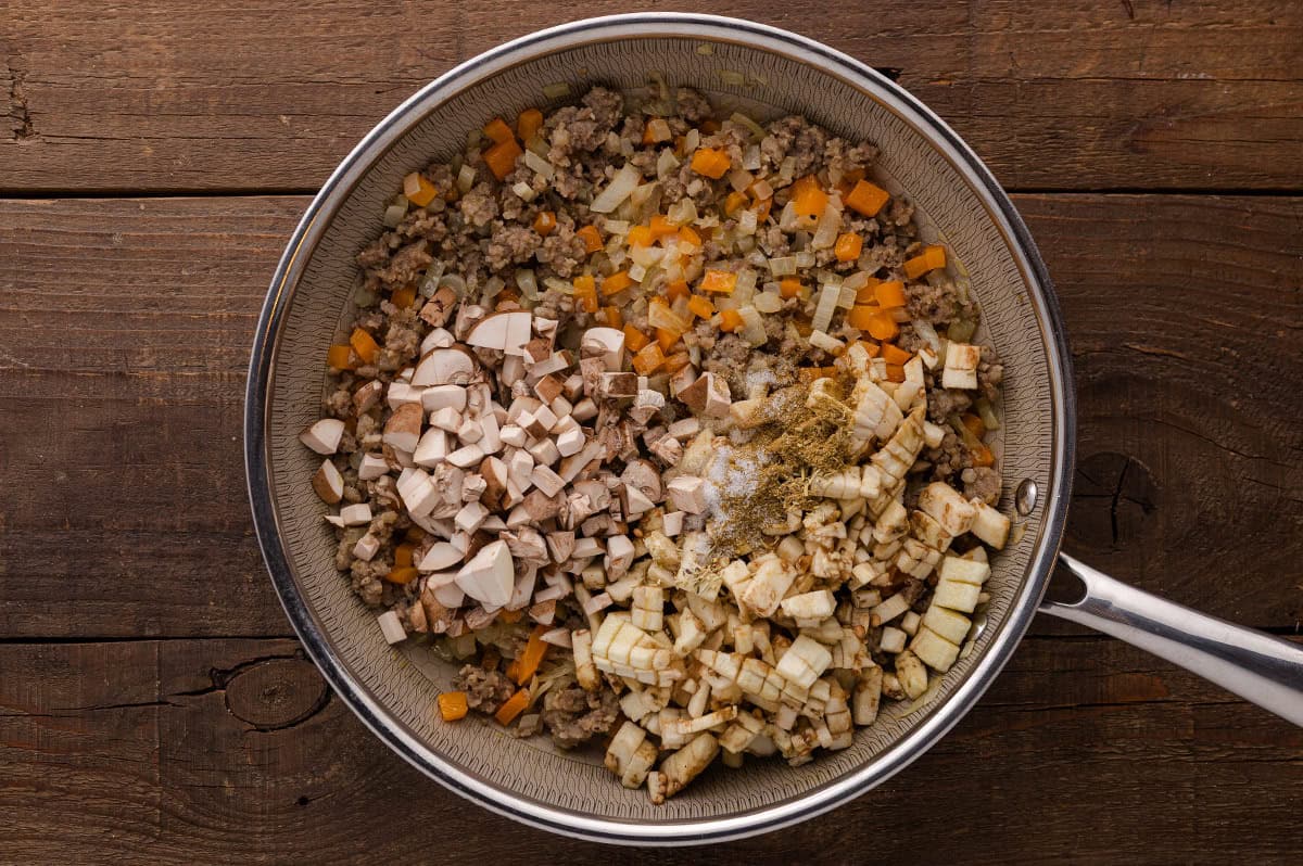 Sautéed onions, sausage, onion and chopped mushrooms cooking in a skillet.