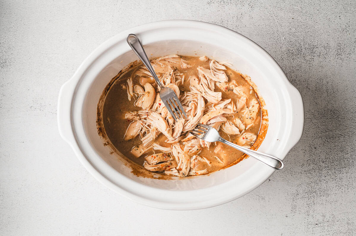 Shredded chicken mixed into the rich gravy inside the slow cooker.