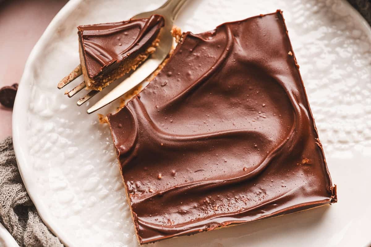 A hand holding a buckeye bar above a plate with more bars stacked in the background, highlighting the creamy texture.