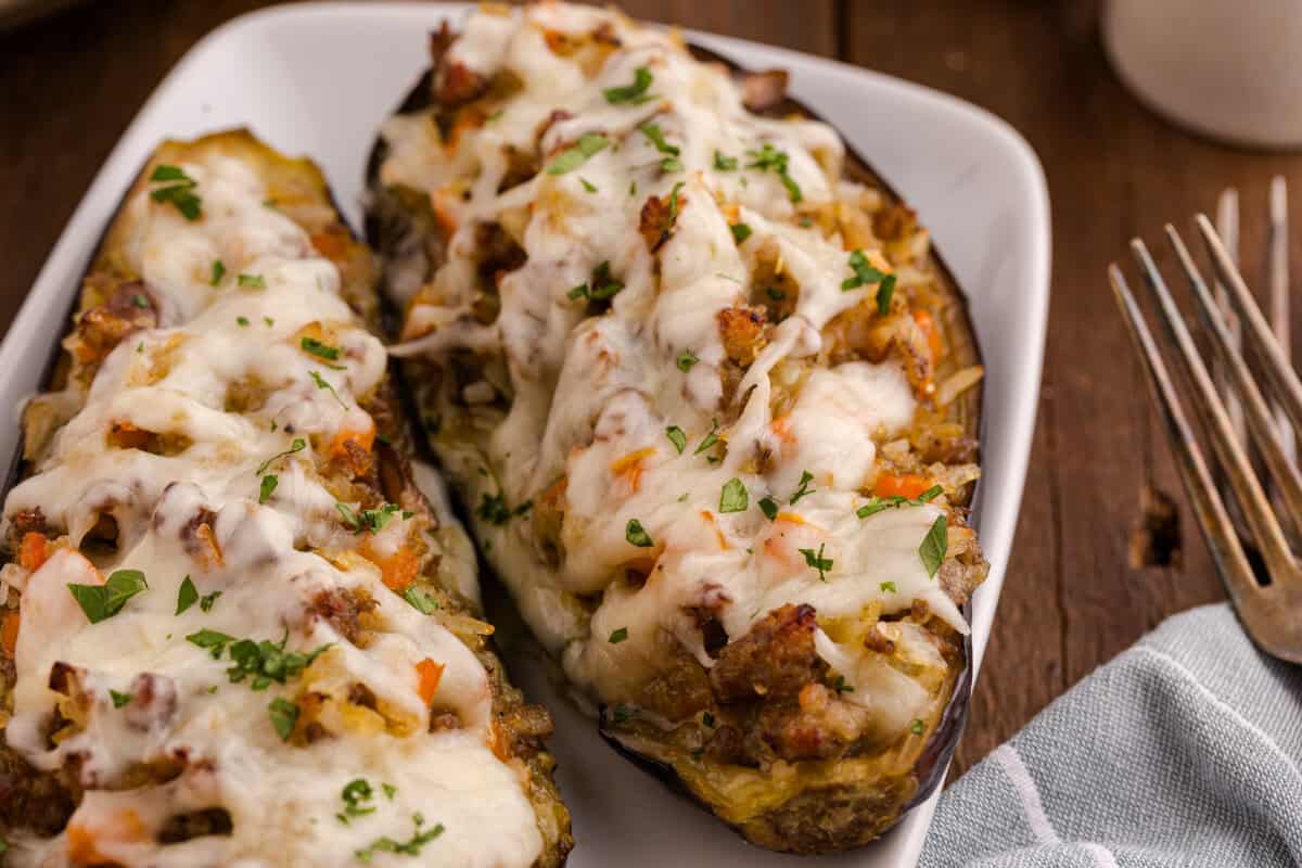 Close-up of stuffed eggplant served with a fork and knife on a white plate, garnished with parsley.