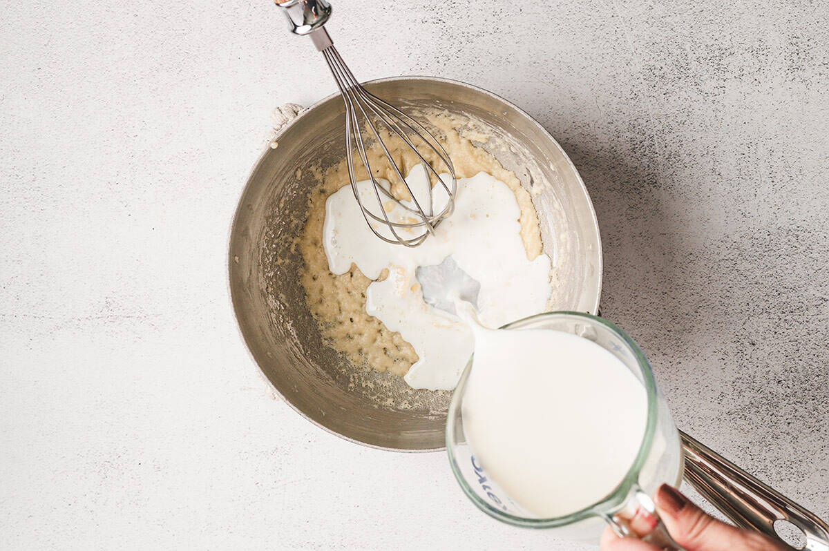 Milk being slowly poured into the roux, whisking to combine.