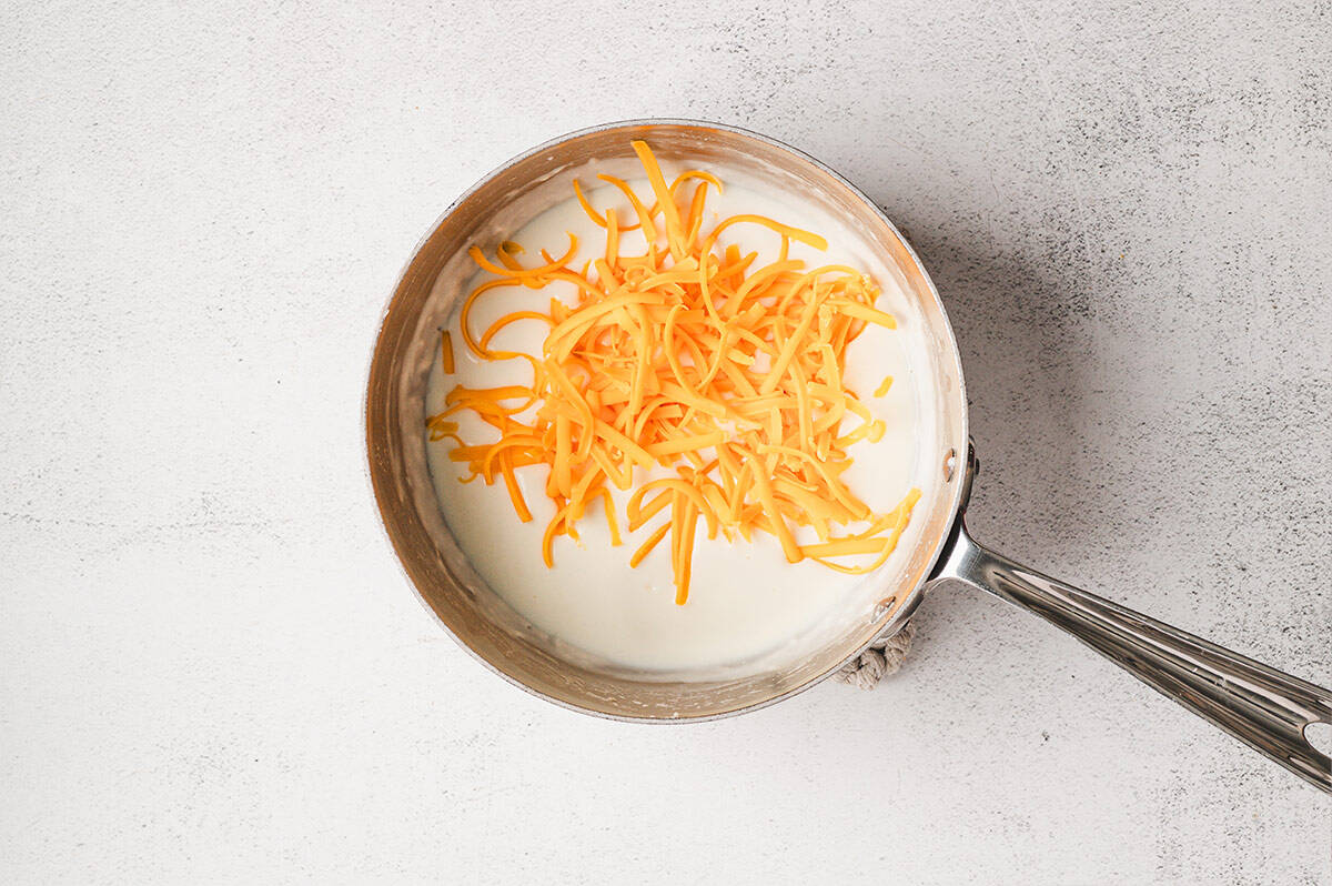 Shredded sharp cheddar cheese added to the thickened milk mixture.