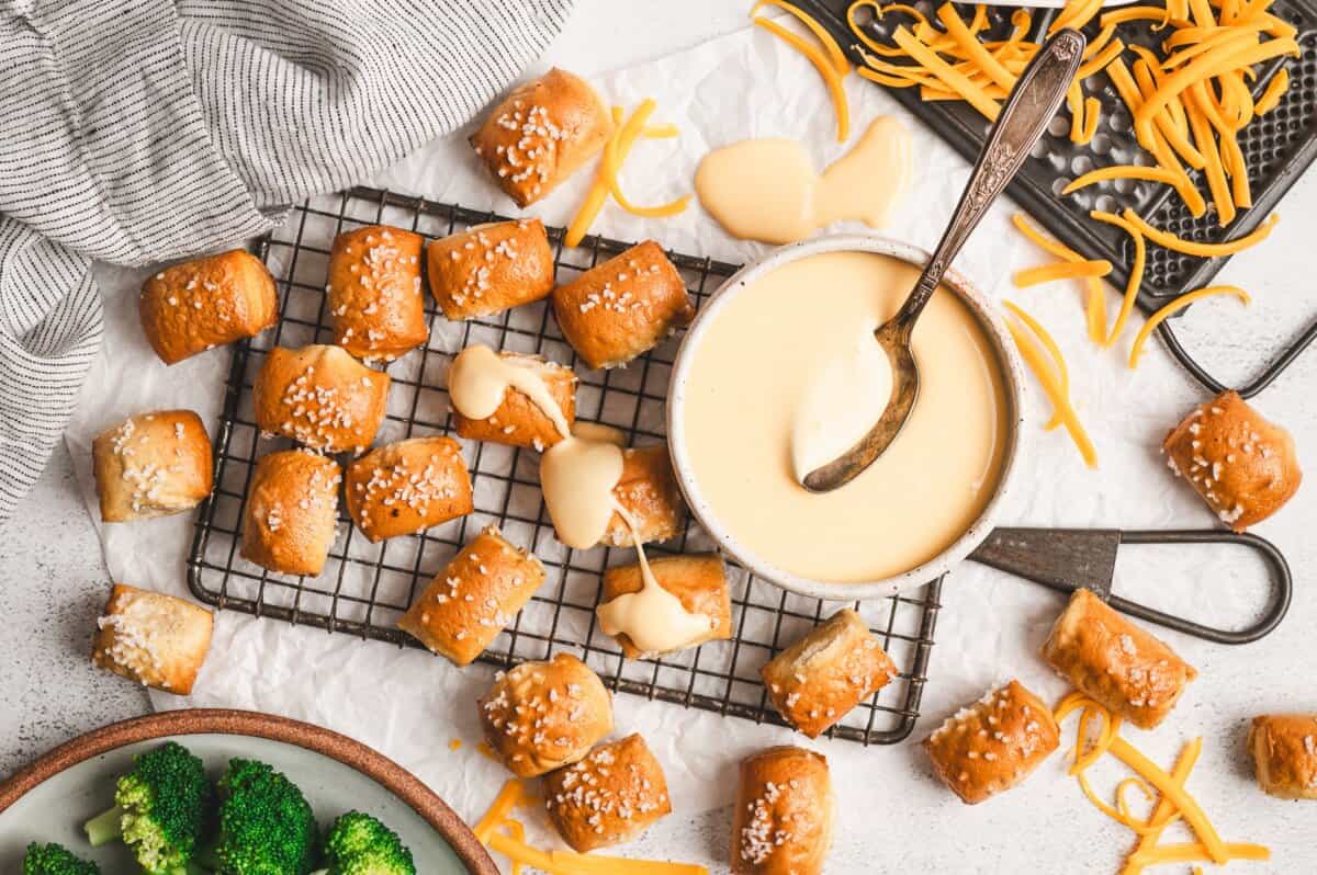 A bowl of creamy cheese sauce with a spoon, surrounded by ingredients like shredded cheese and milk.