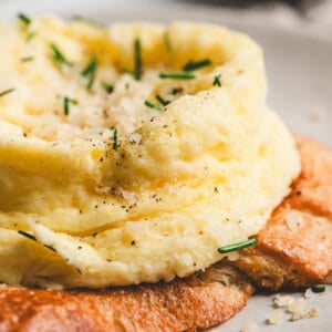 Close-up of a fluffy microwave soufflé-style egg topped with Parmesan and chives, served over toasted bread.