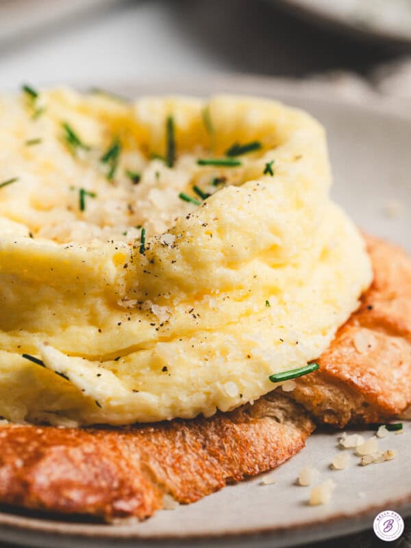 Close-up of a fluffy microwave soufflé-style egg topped with Parmesan and chives, served over toasted bread.