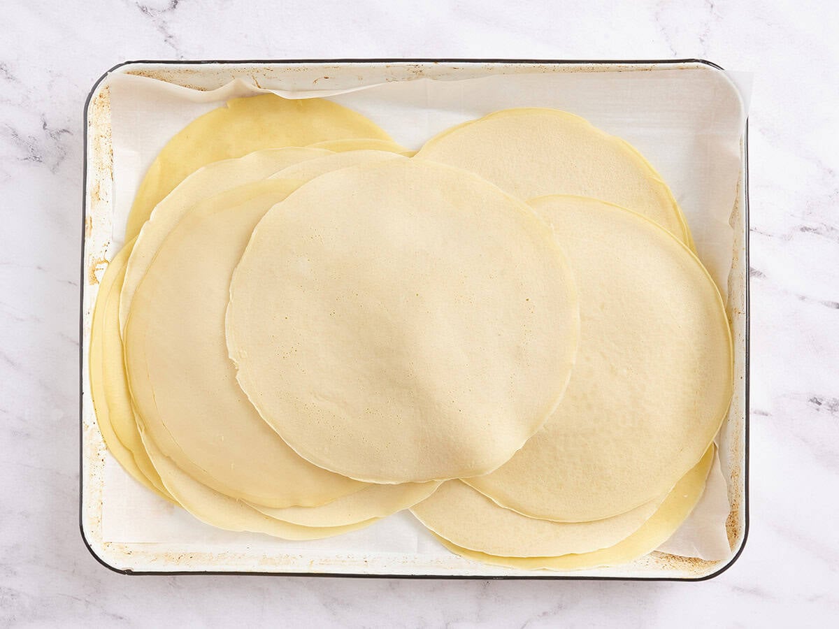 A tray lined with parchment paper holding a stack of plain cooked crepes, ready for assembly.