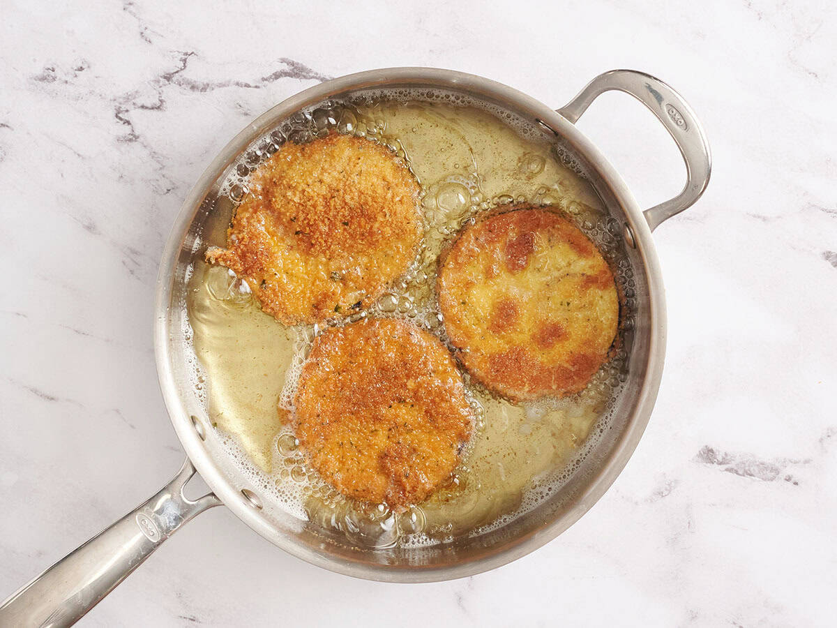 Golden-brown breaded eggplant slices frying in hot oil.