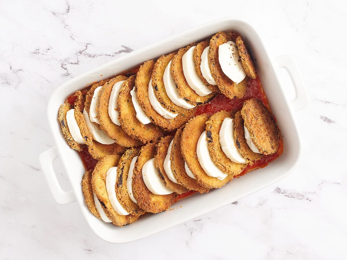 Layered mozzarella cheese and fried eggplant slices cascading in a baking dish.