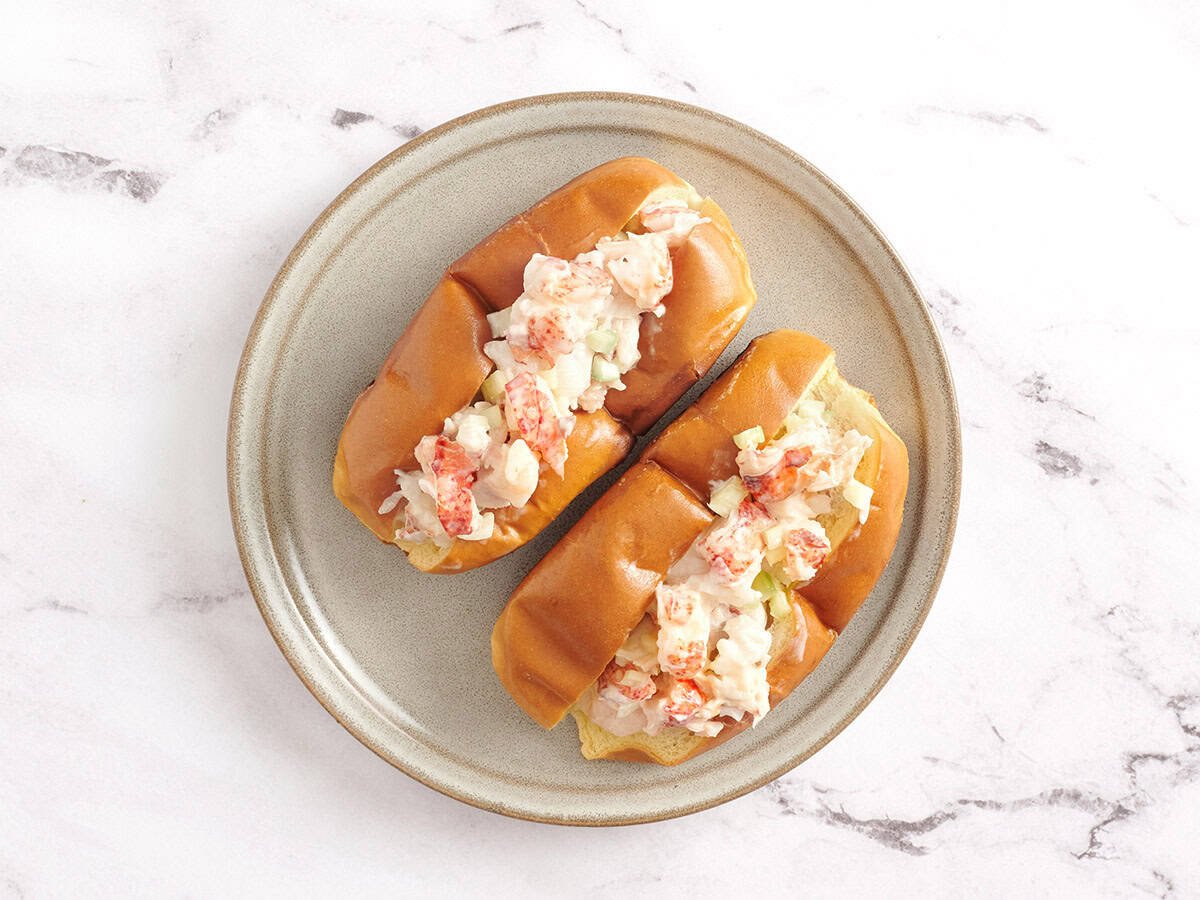 Two lobster rolls filled with lobster salad on a round ceramic plate.