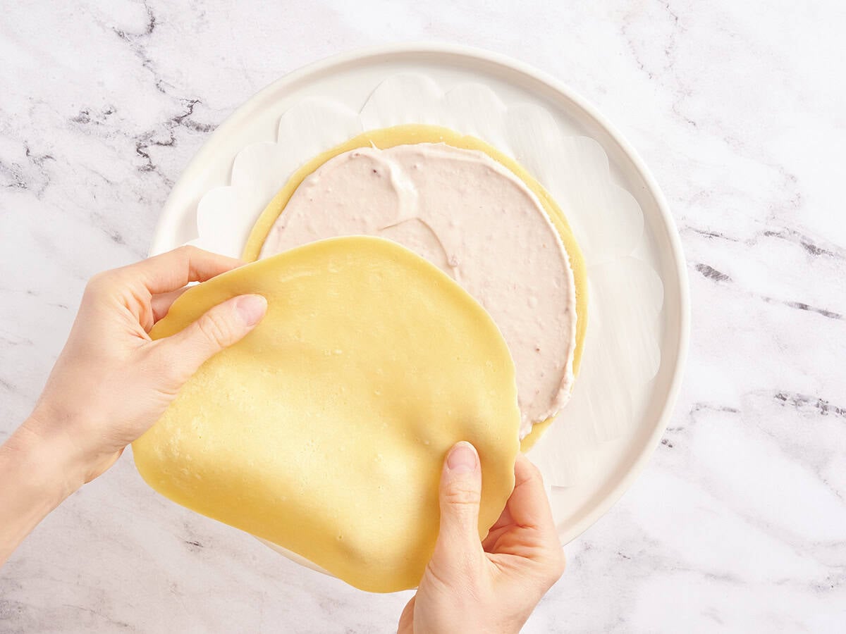 Placing a fresh crepe on top of a layer already covered with raspberry cream filling.