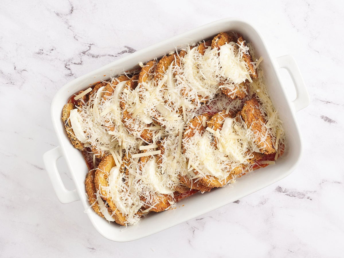 Shredded Parmesan cheese over the mozzarella and eggplant layers in a white baking dish.