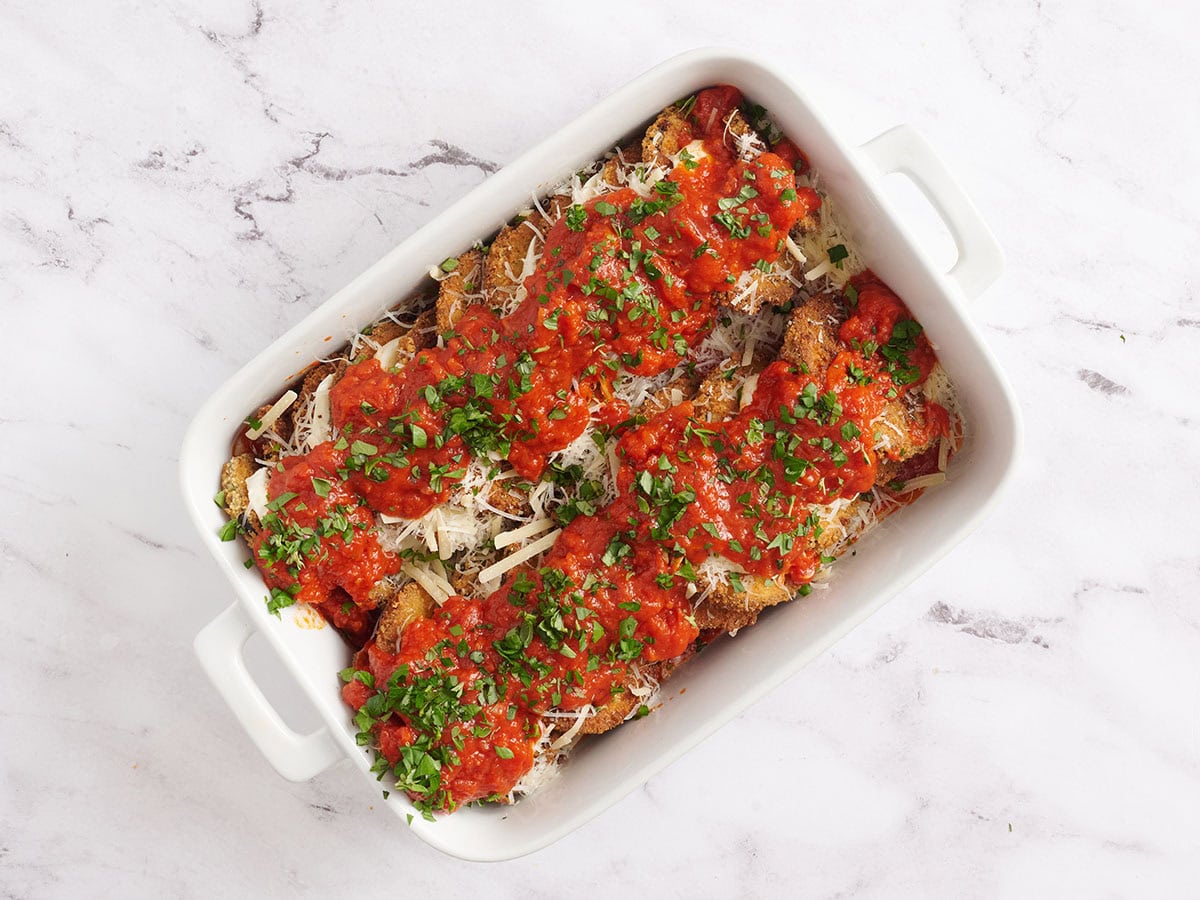 Fresh herbs scattered on top of the layered eggplant parmesan dish.