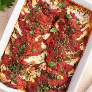 Golden-brown baked Eggplant Parmesan layered with marinara and melted cheese, garnished with fresh herbs in a white baking dish.