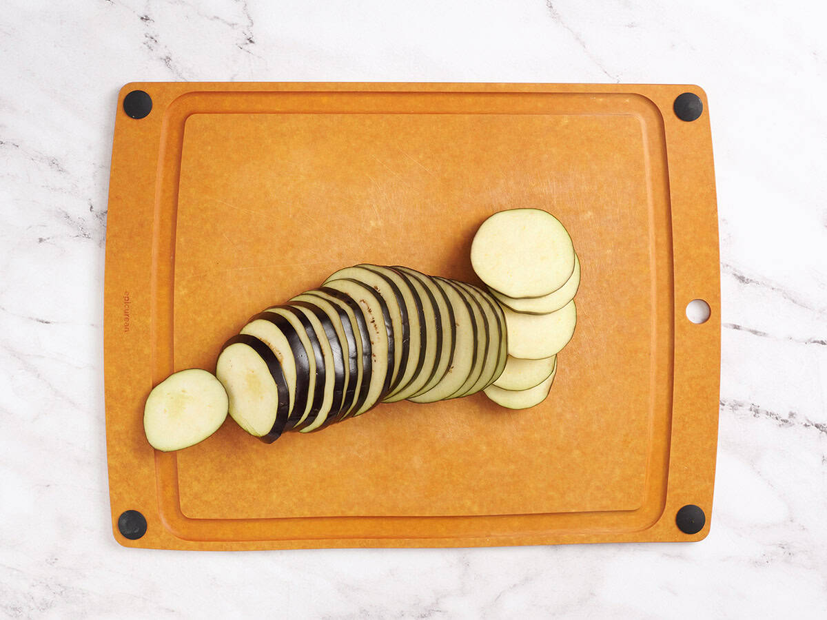Eggplants cut into even ½-inch rounds, arranged on a wooden cutting board.