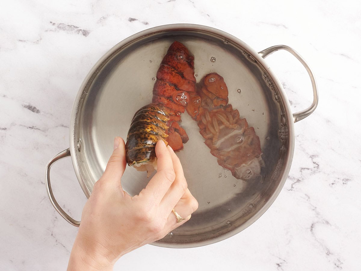 Two lobster tails being placed in a large pot with boiling water.