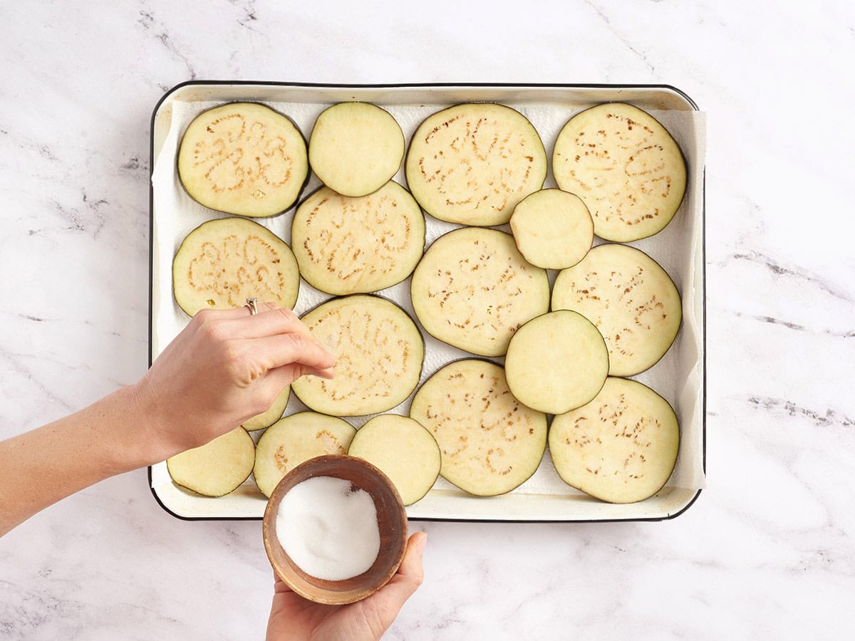 Raw eggplant rounds sprinkled with salt and arranged in a colander to draw out excess moisture.
