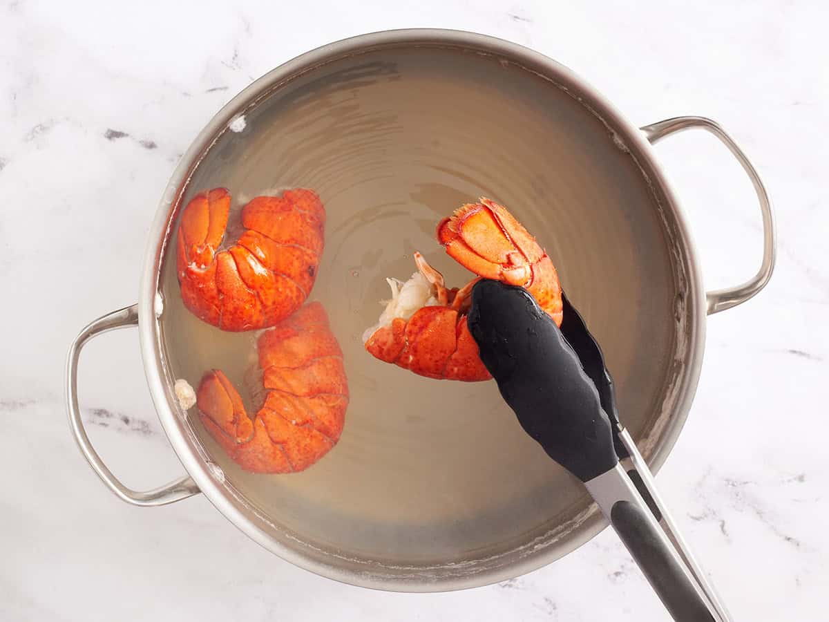 Cooked lobster tail being lifted out of a pot with tongs.