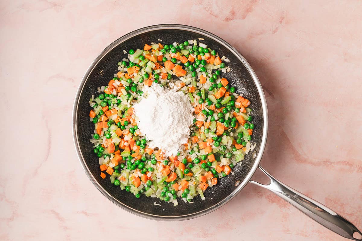 Onions and celery sautéing in a skillet with flour sprinkled over the vegetables to create a roux.
