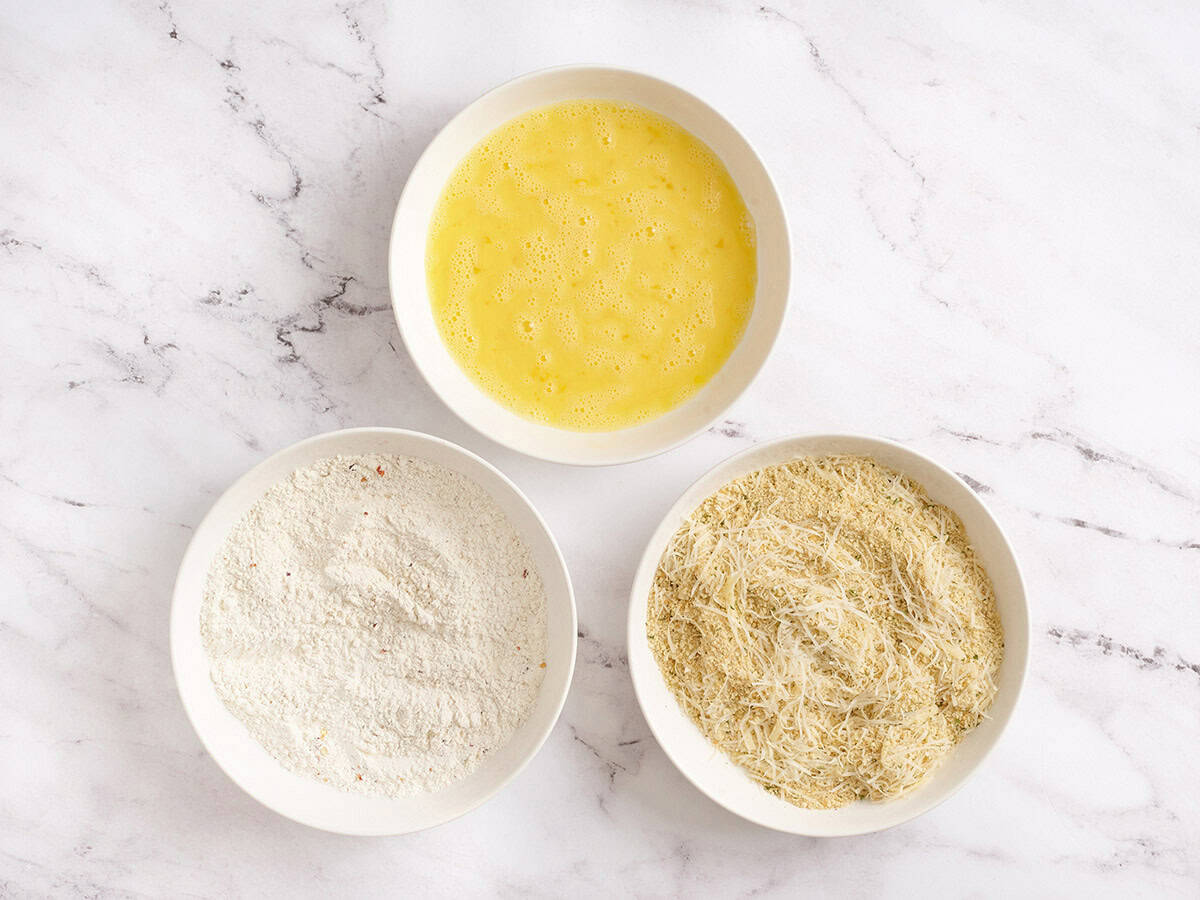 Three shallow bowls filled with flour, beaten eggs, and a breadcrumb mixture, ready for dredging.