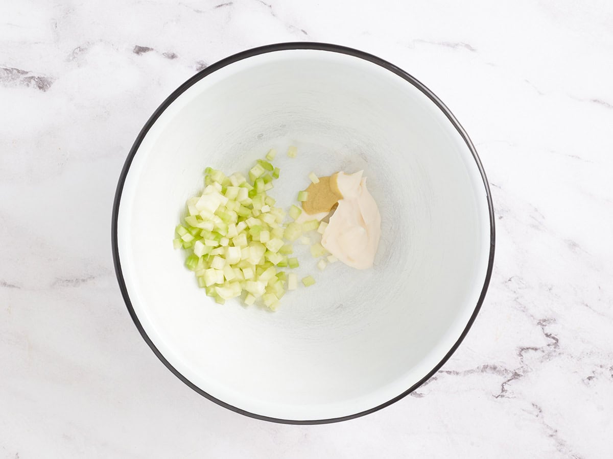 Mixing bowl filled with mayonnaise, diced celery, mustard, and salt for lobster roll filling.
