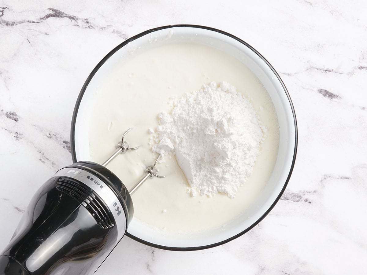 A bowl of heavy cream with powdered sugar on top, ready to be whipped with an electric hand mixer.