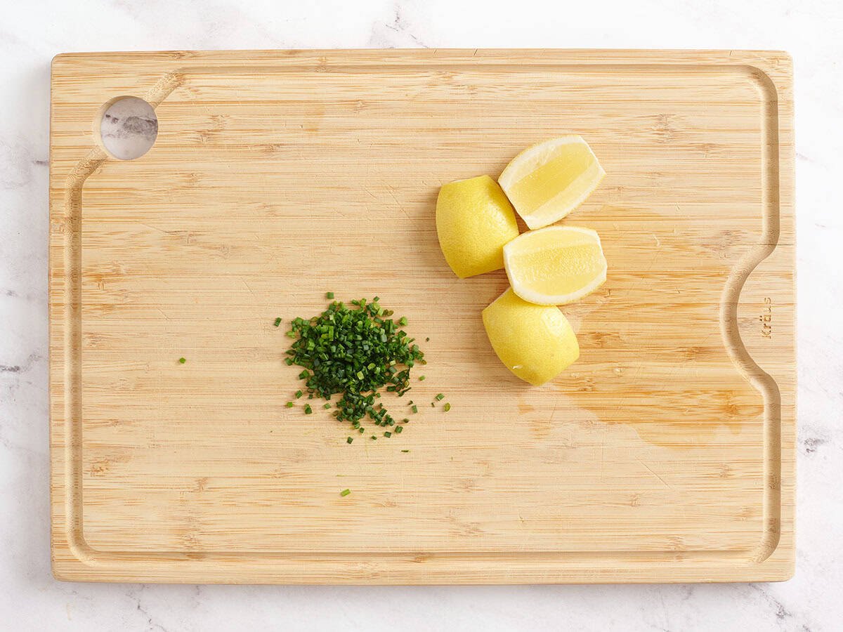 Finely chopped parsley and lemon quarters on a cutting board, ready to be used as garnish.