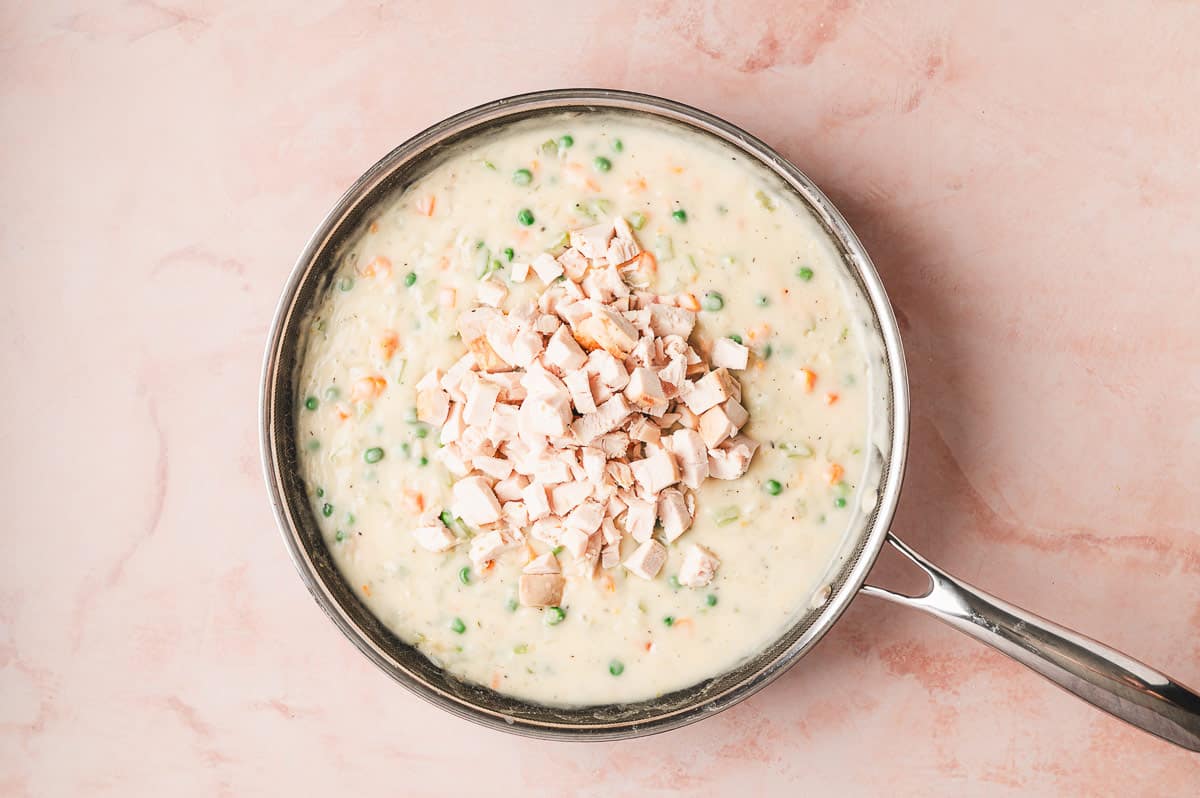 Shredded cooked chicken and frozen peas added into the creamy sauce mixture in the skillet.