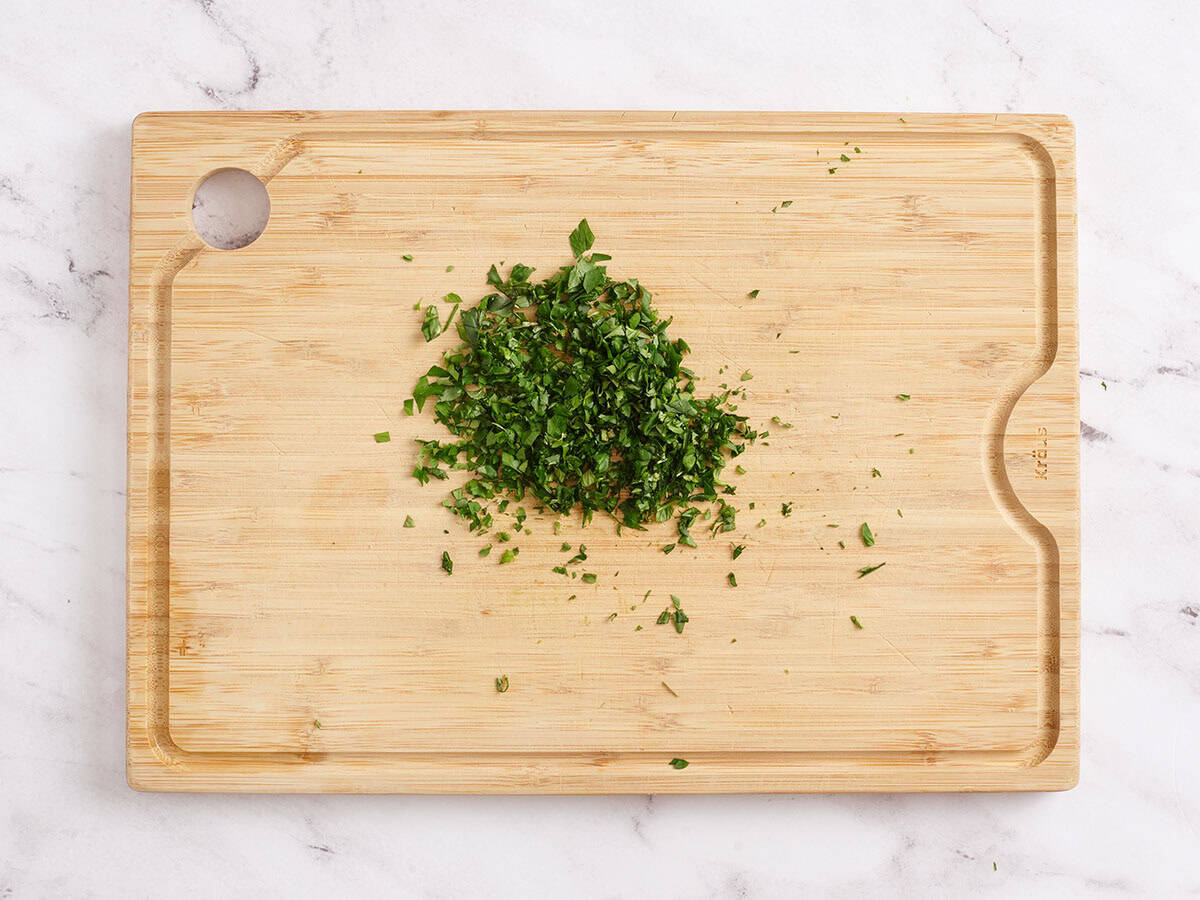 Chopped fresh basil and parsley on a wooden board.