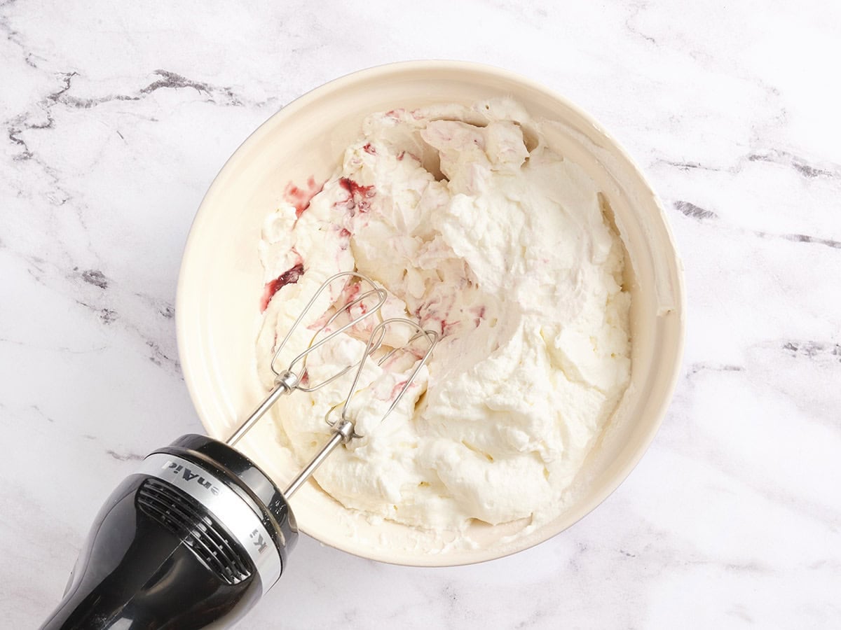 Cream cheese, raspberry jam, and whipped cream being blended together with an electric hand mixer.