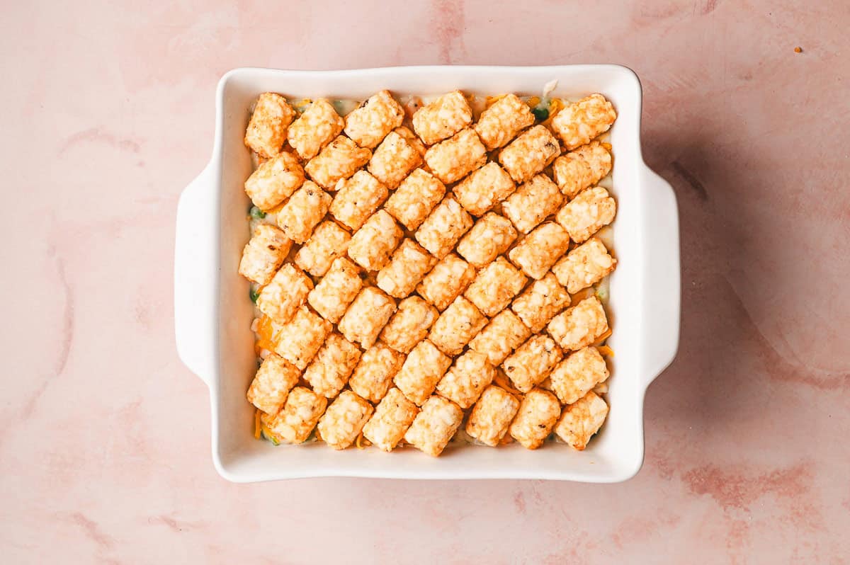 Rows of frozen tater tots being neatly arranged on top of the chicken filling in the baking dish.