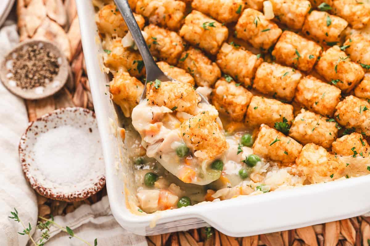 A serving of chicken tot pie scooped from the dish, revealing the creamy filling beneath the tater tots.