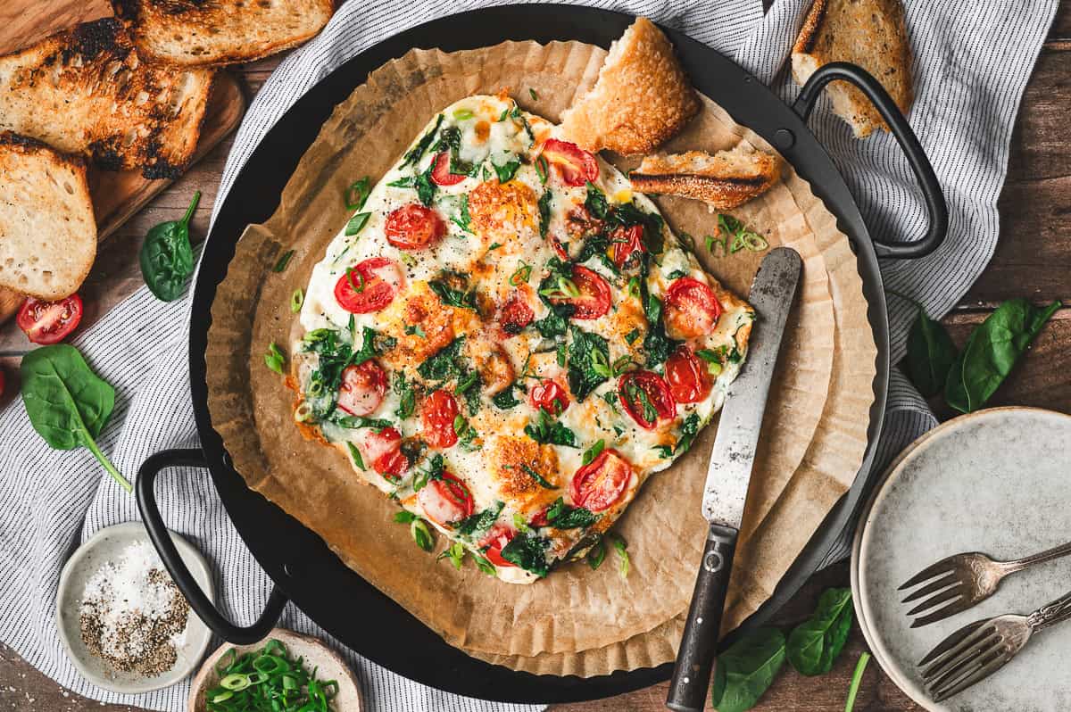 Finished frittata on parchment paper with toasted bread on the side, ready to slice and serve.