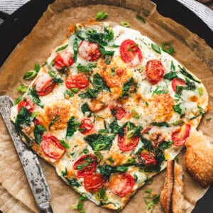 Overhead view of an air fryer egg frittata topped with spinach, cherry tomatoes, and melted mozzarella, served with toasted bread.