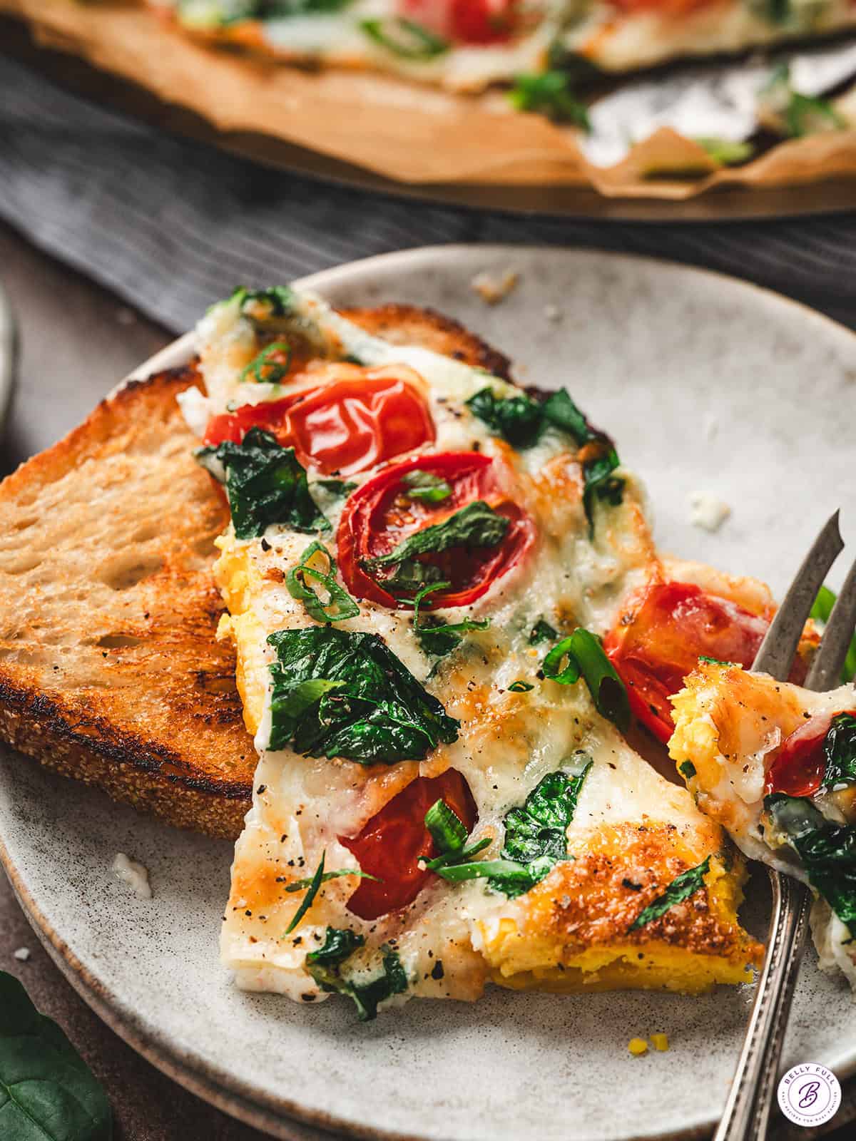 Close-up of a frittata slice being lifted with a serving spatula, showing gooey cheese, tomatoes, and spinach.